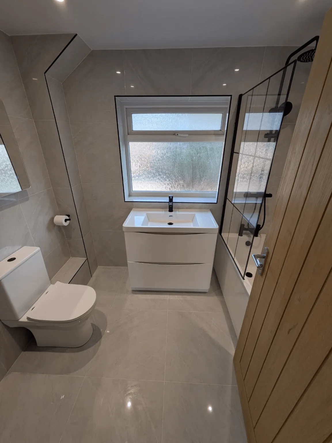 Compact bathroom with a white vanity beneath the window and black-framed bath screen
