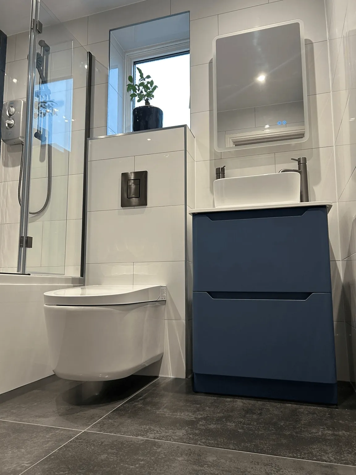 Compact shower room with a blue vanity, countertop basin and wall-hung toilet