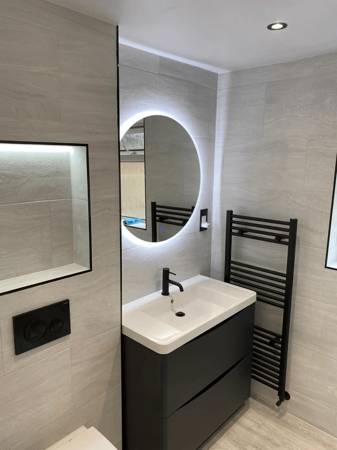 Bathroom vanity beside a black towel radiator and illuminated recessed shelf