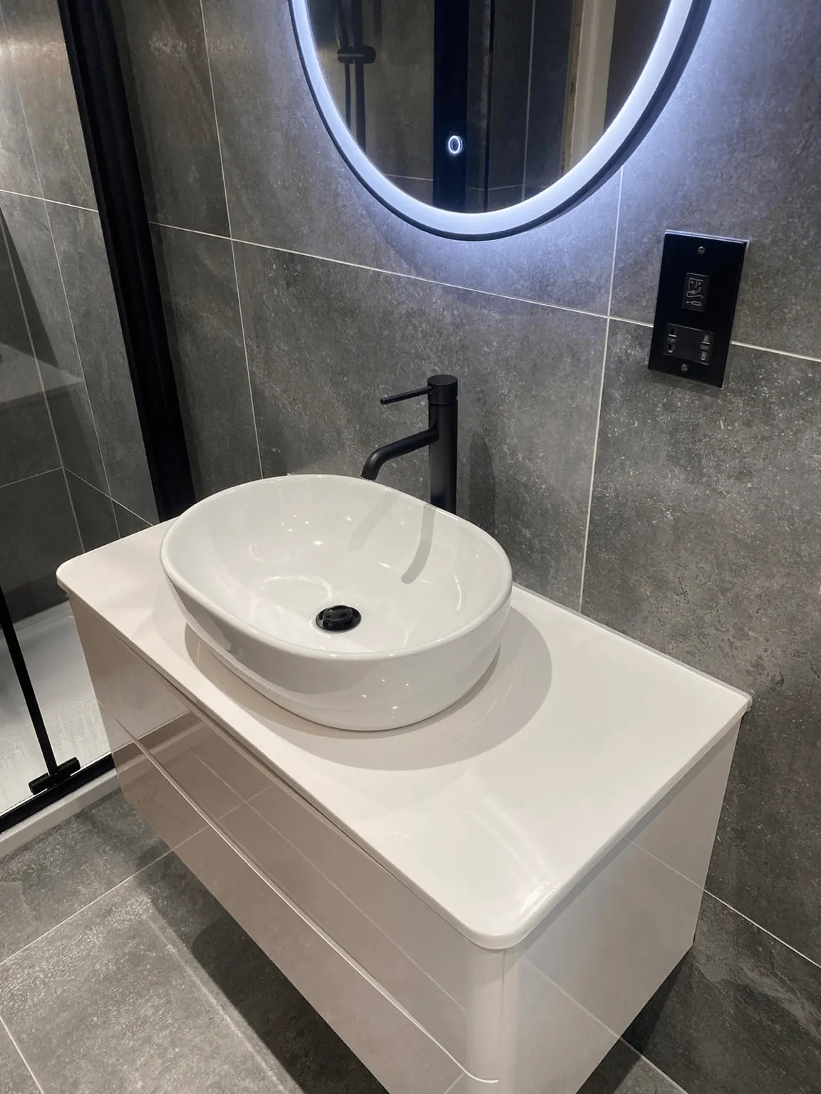 Round countertop basin with a black tap against grey bathroom tiles