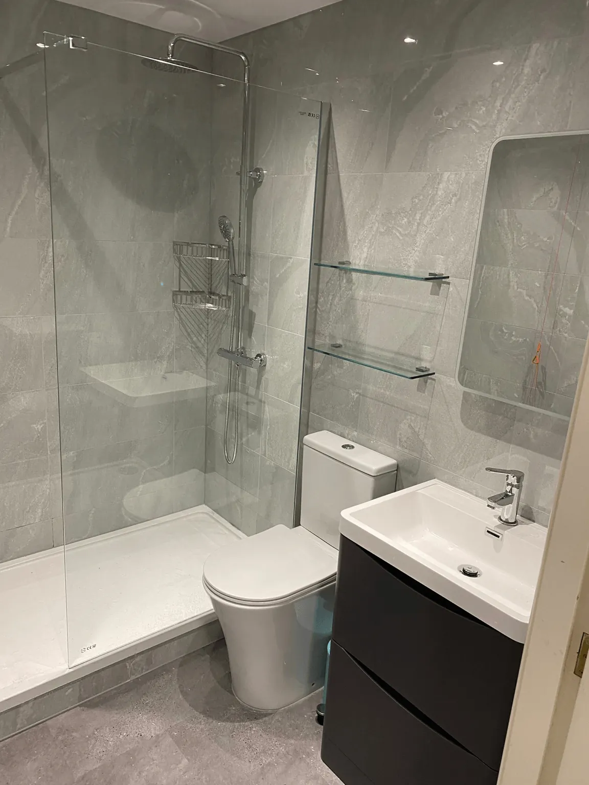 Grey tiled shower room with a glass screen, toilet and dark vanity