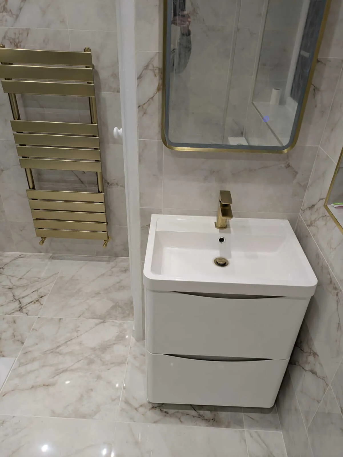 White floating vanity with a gold-coloured tap and matching towel radiator