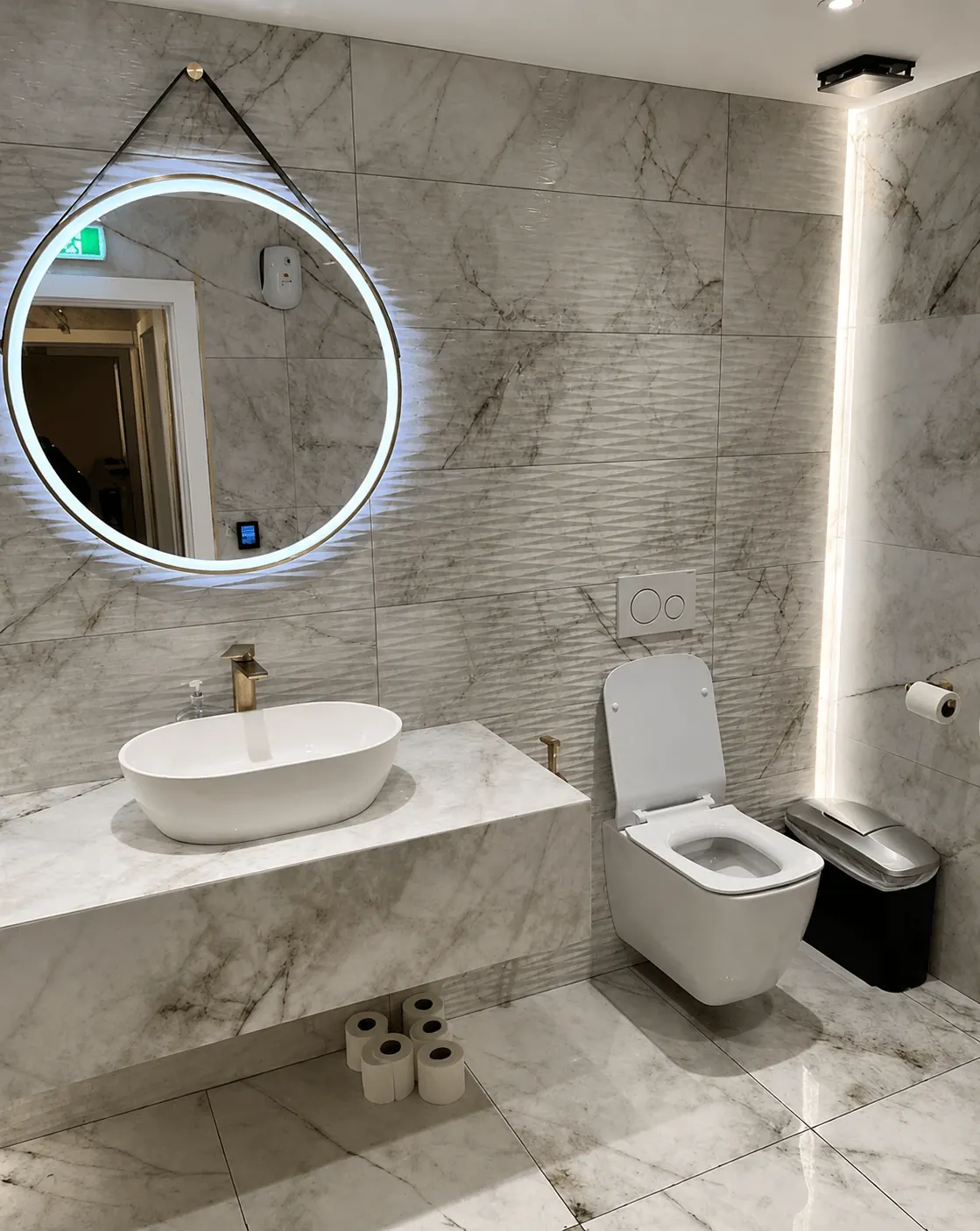 Bathroom with a round illuminated mirror, countertop basin and wall-hung toilet