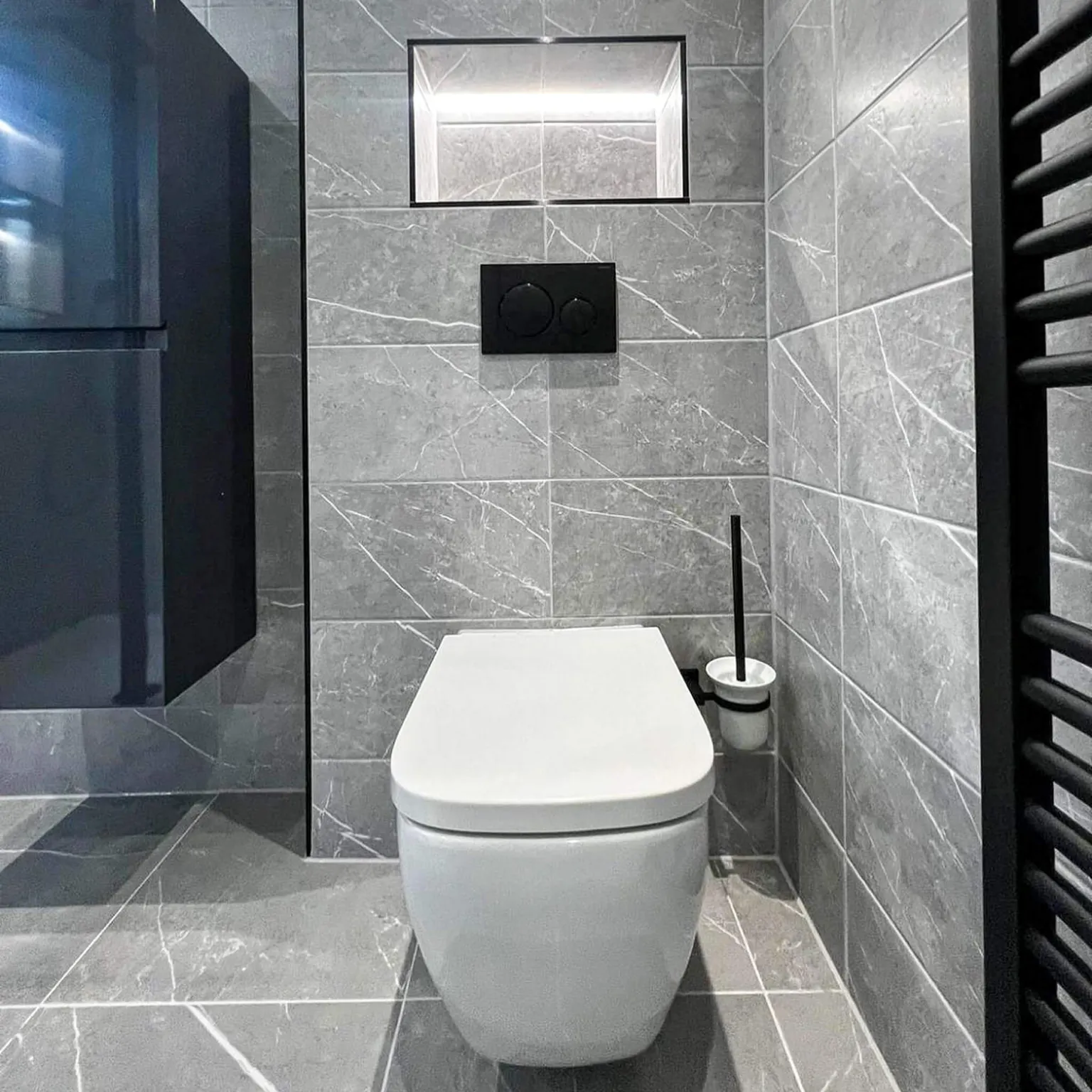 Wall-hung toilet and black towel radiator in a grey tiled ensuite