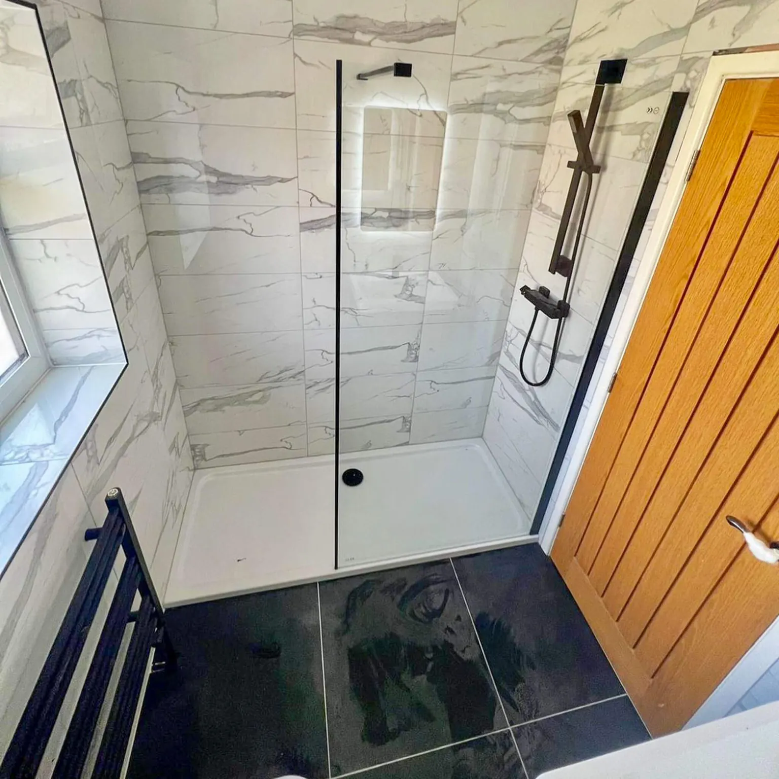 Compact ensuite shower with marble-effect walls and black fittings