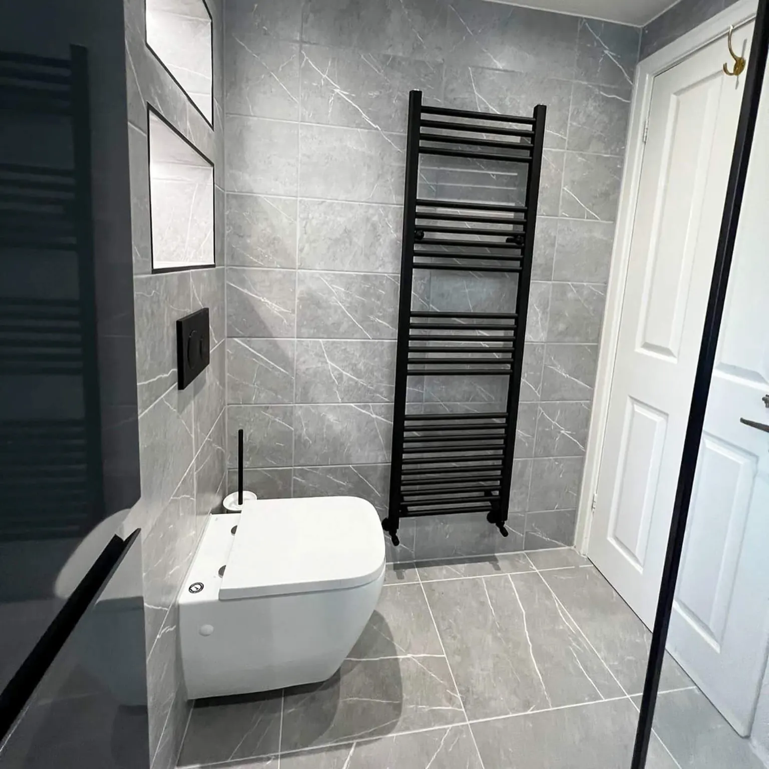 Grey tiled ensuite with a wall-hung toilet and tall black towel radiator