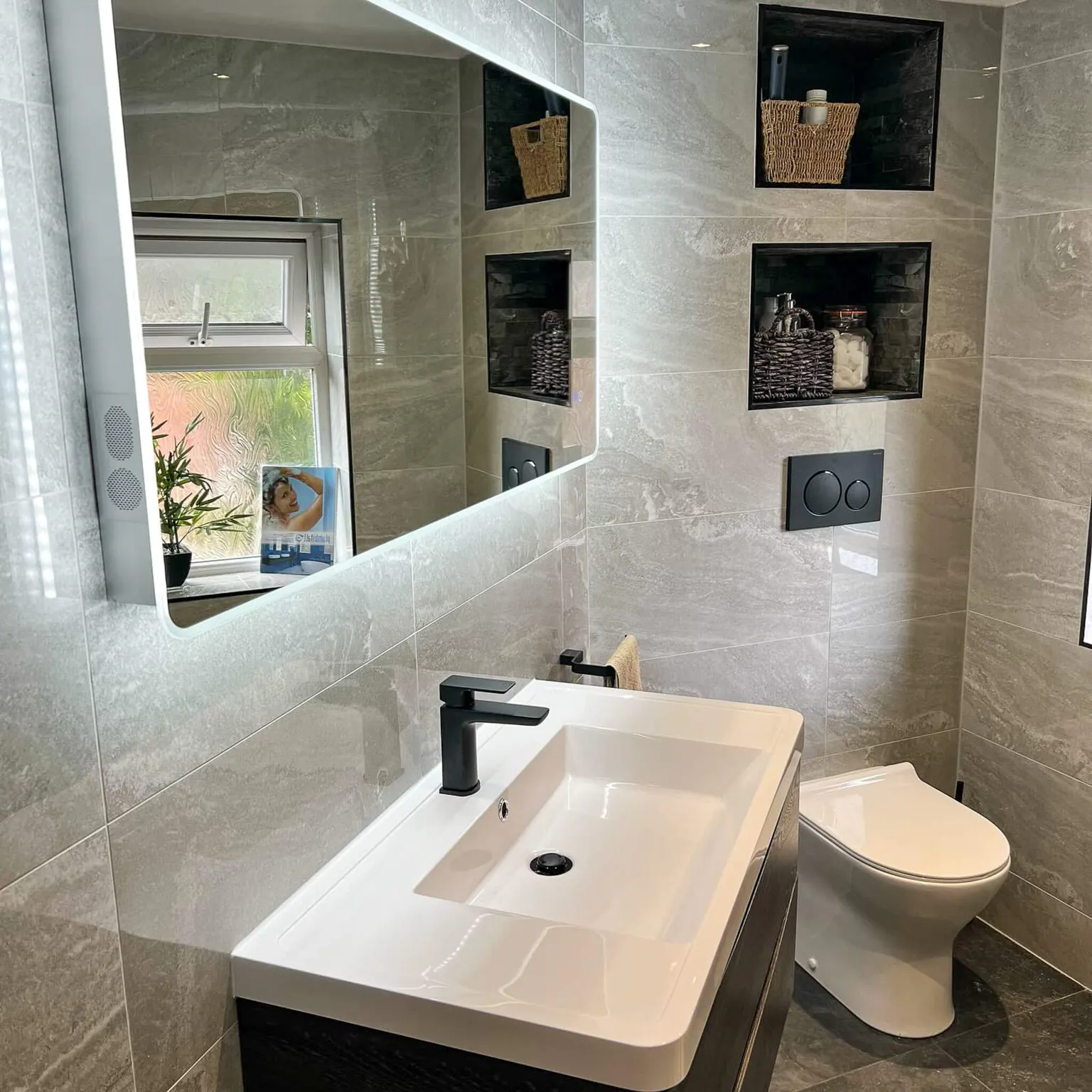 Ensuite basin beneath an illuminated mirror beside recessed storage shelves