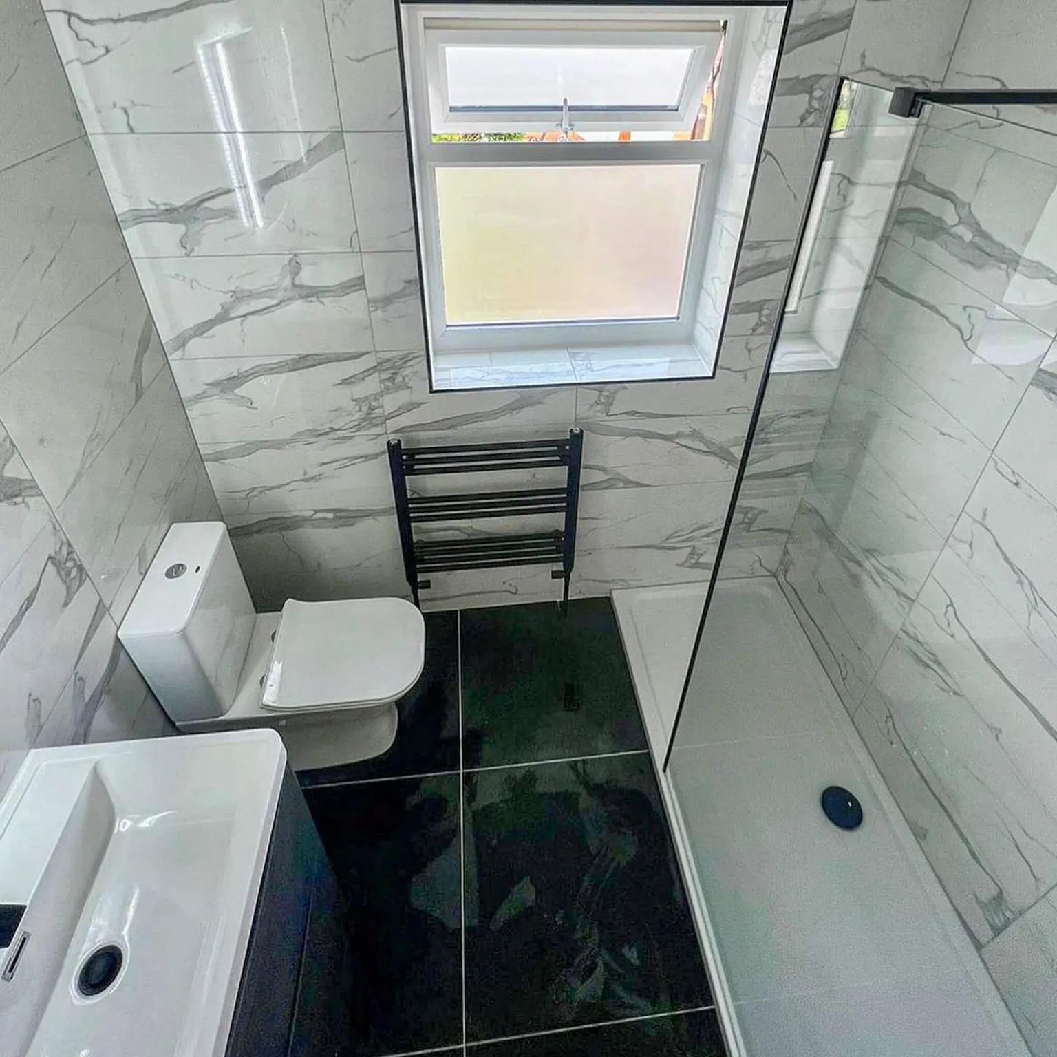 Compact ensuite with marble-effect walls, dark floor and glass shower screen