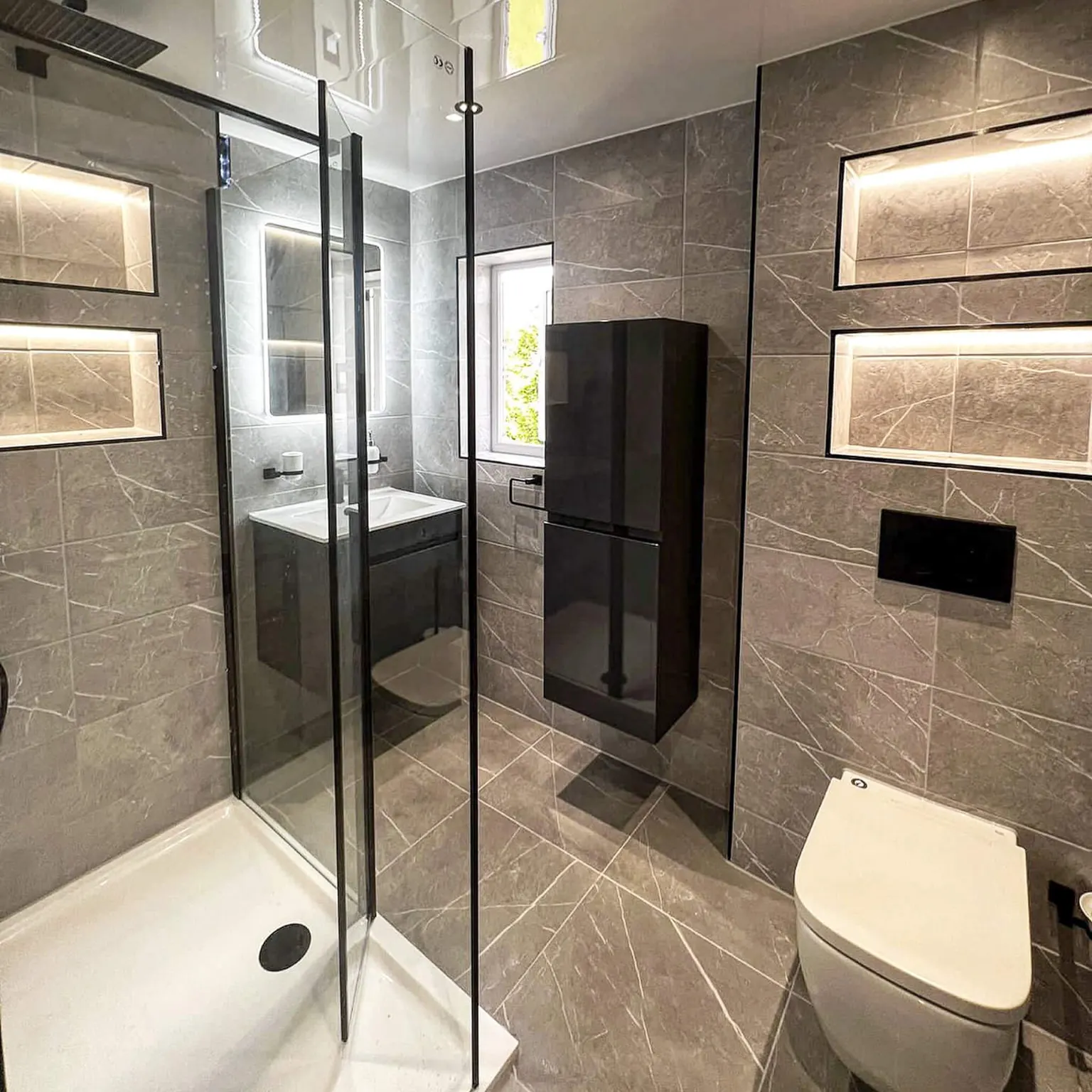 Grey tiled ensuite with illuminated storage recesses and a tall wall cabinet