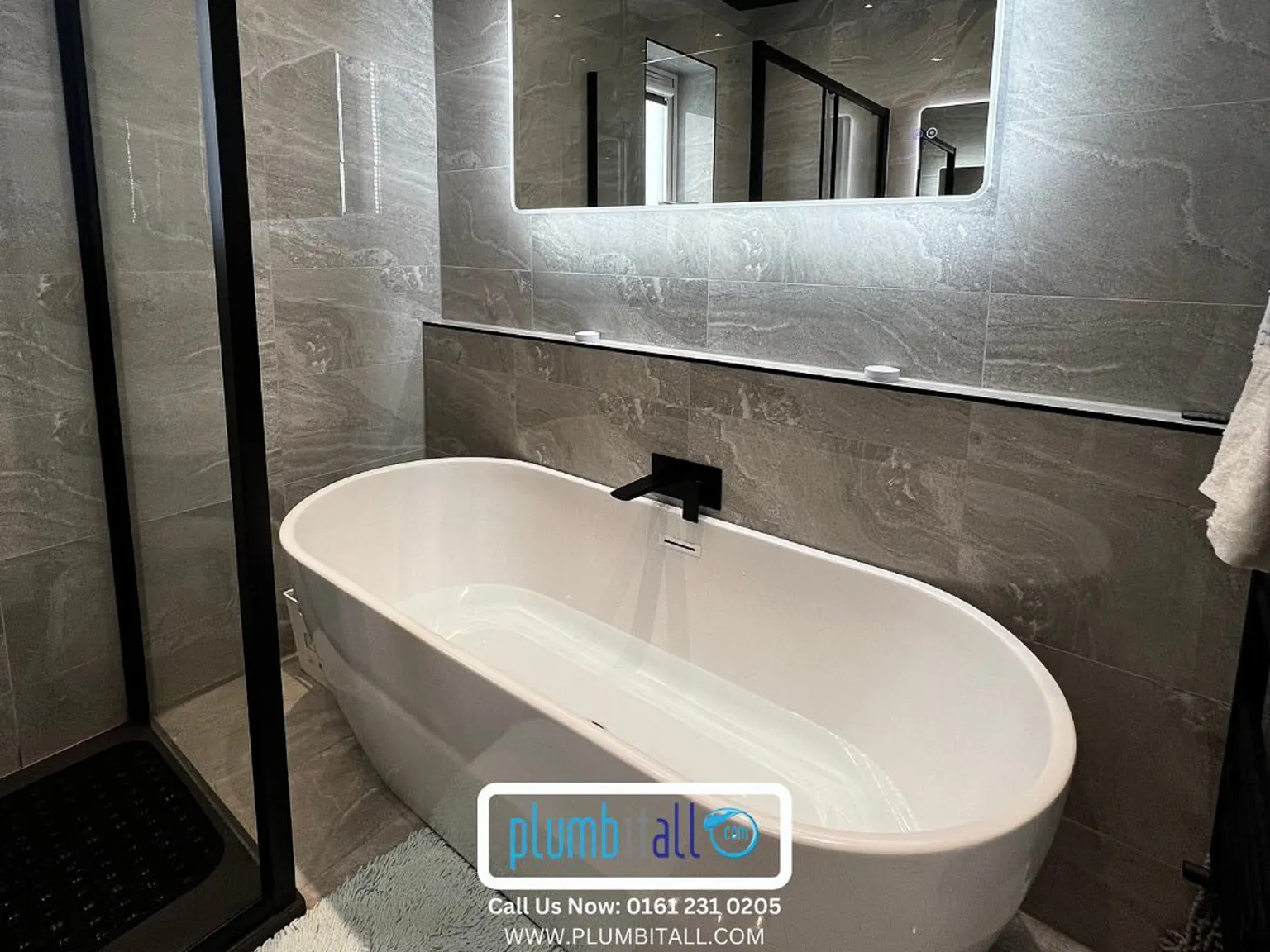 Freestanding oval bath beneath a wide illuminated bathroom mirror