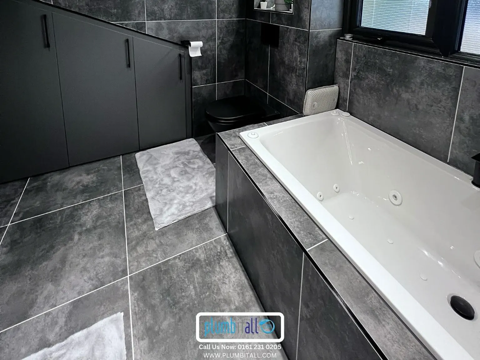 Dark tiled family bathroom with a fitted bath and glass shower screen