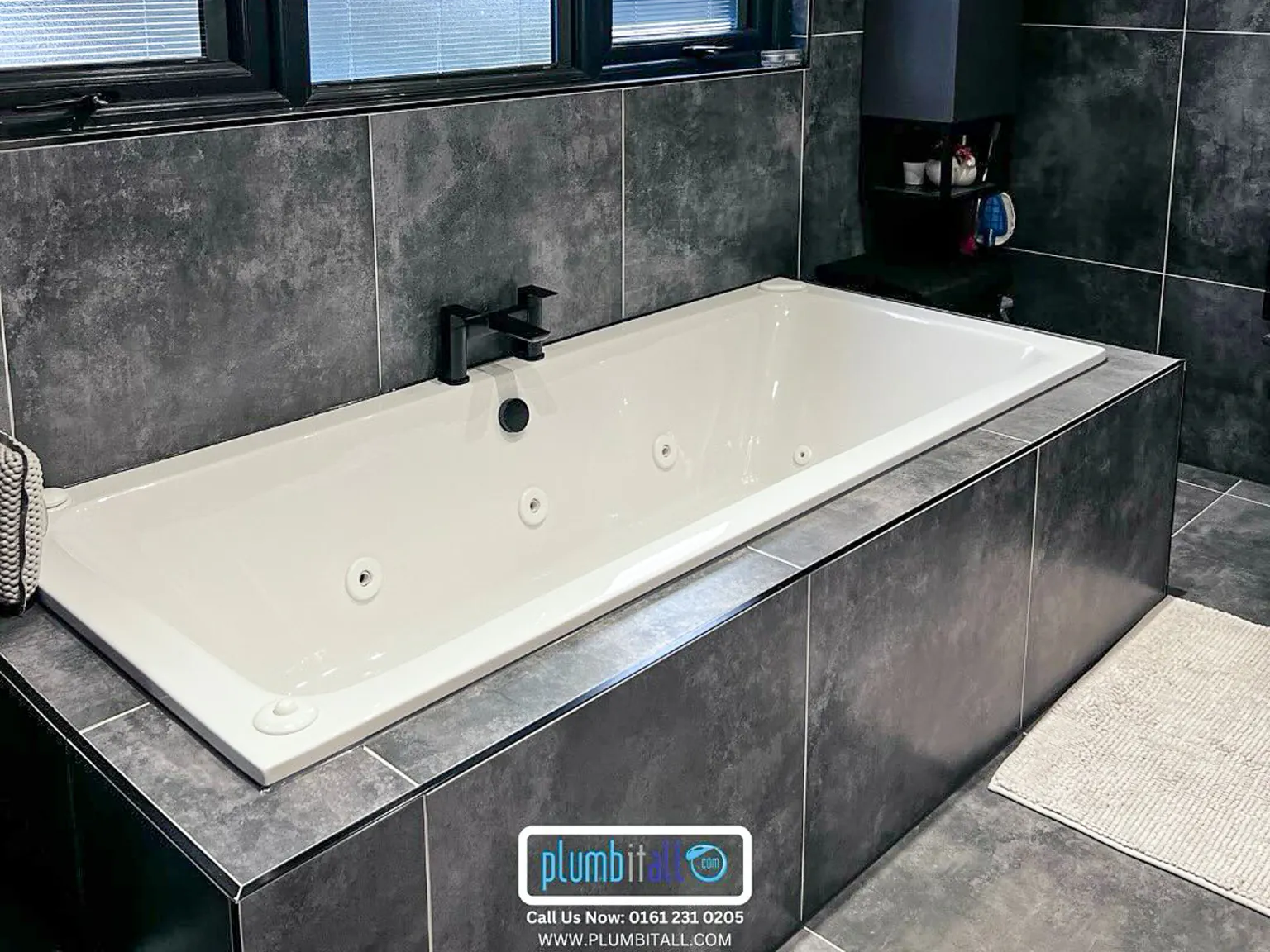 Fitted bath with black tap and dark grey tiled surround